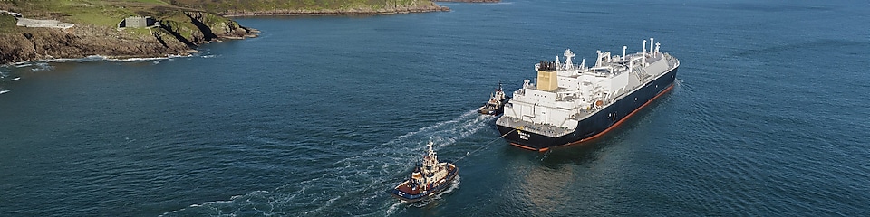 Cargo ship in the middle of water passing land.